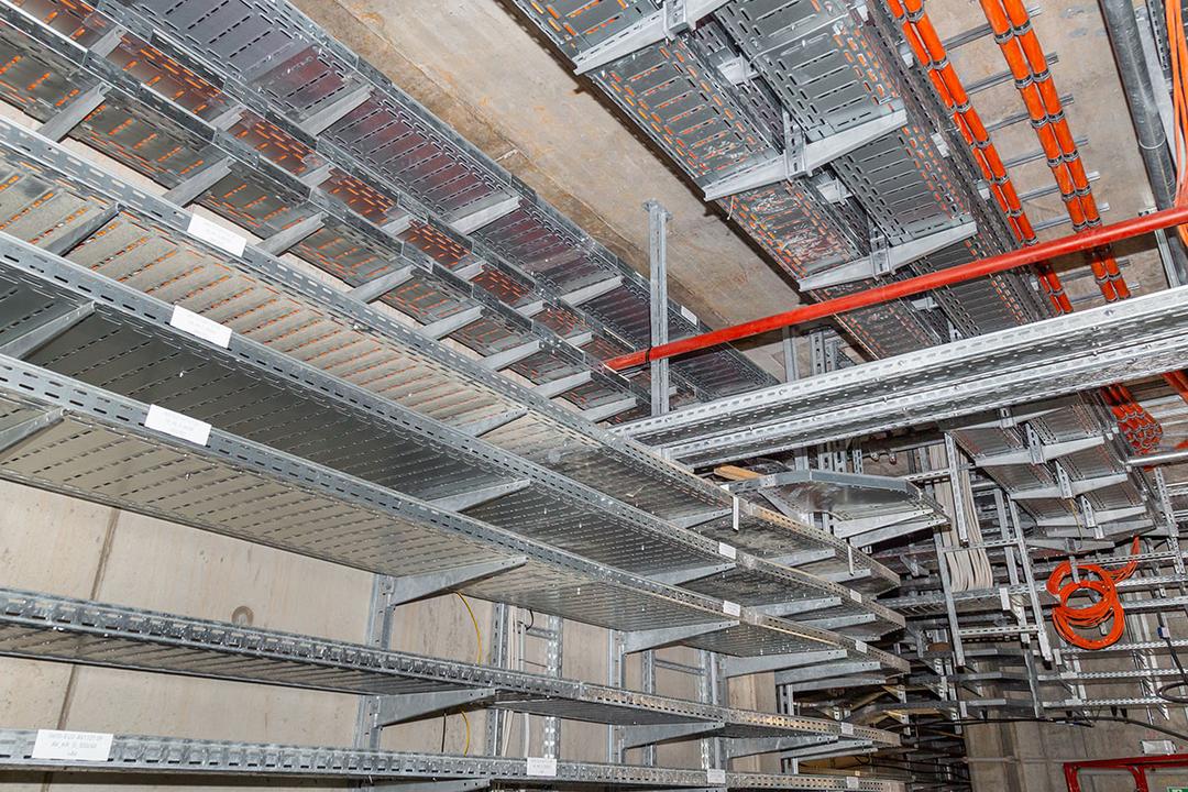 Kabelrinnen mit orangefarbenen Kabeln befestigt an Betondecke und Betonwand in einem Technikraum