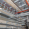 Kabelrinnen mit orangefarbenen Kabeln befestigt an Betondecke und Betonwand in einem Technikraum