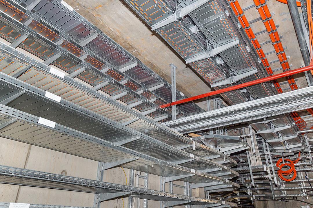 Kabelrinnen mit orangefarbenen Kabeln befestigt an Betondecke und Betonwand in einem Technikraum