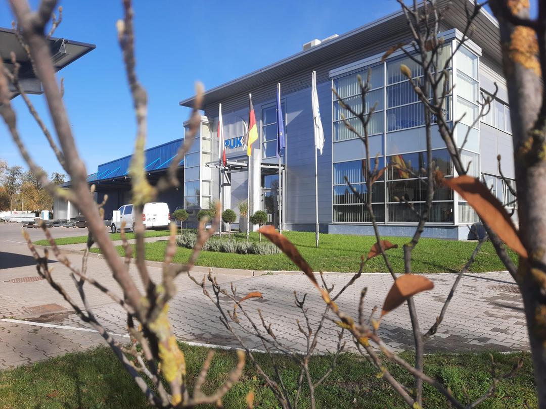 EL-PUK Firmengebäude im polnischen Lodz mit Fahnen und moderner Glasfassade, aufgenommen an einem sonnigen Tag.