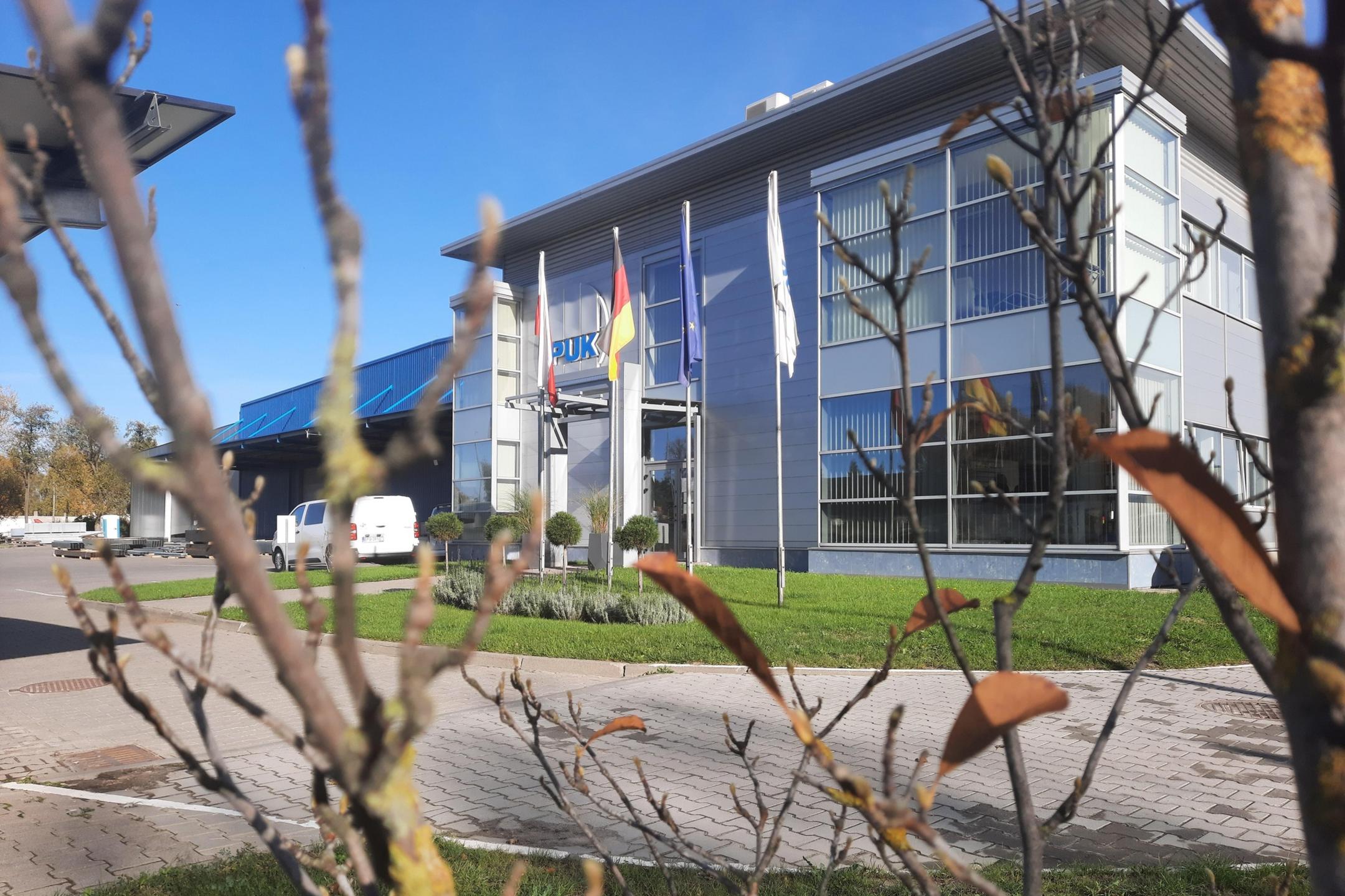 EL-PUK Firmengebäude im polnischen Lodz mit Fahnen und moderner Glasfassade, aufgenommen an einem sonnigen Tag.