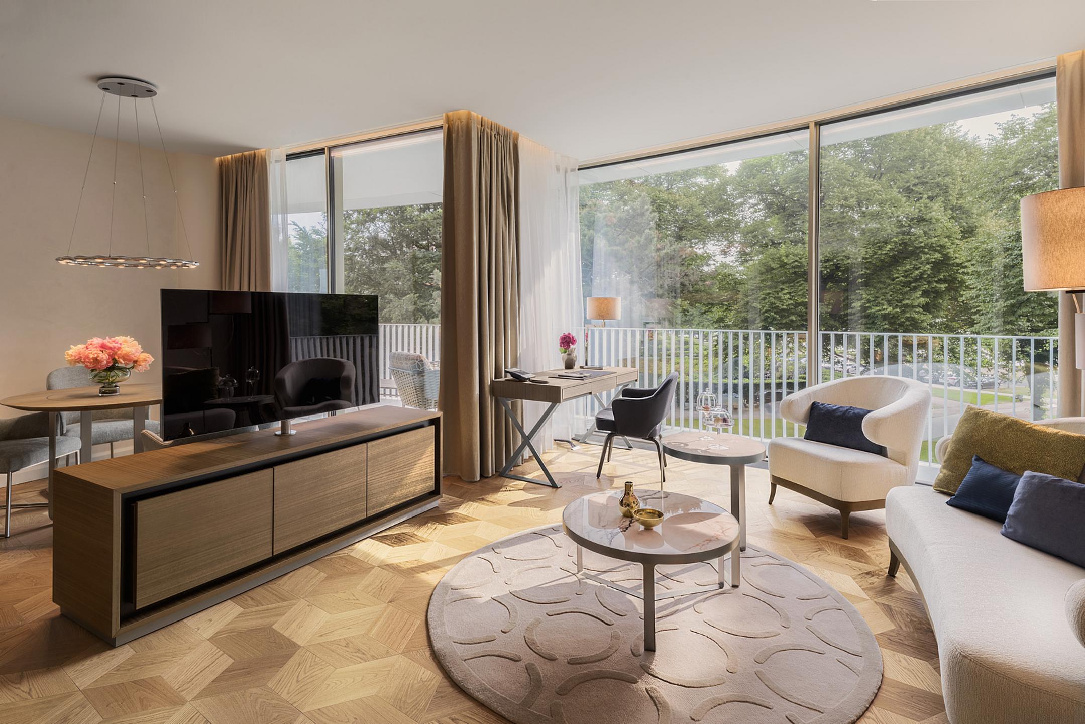 Helles Wohnzimmer mit modernem Design, gemütlicher Sitzecke, Schreibtisch und großen Fenstern mit Balkonblick.