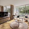 Helles Wohnzimmer mit modernem Design, gemütlicher Sitzecke, Schreibtisch und großen Fenstern mit Balkonblick.