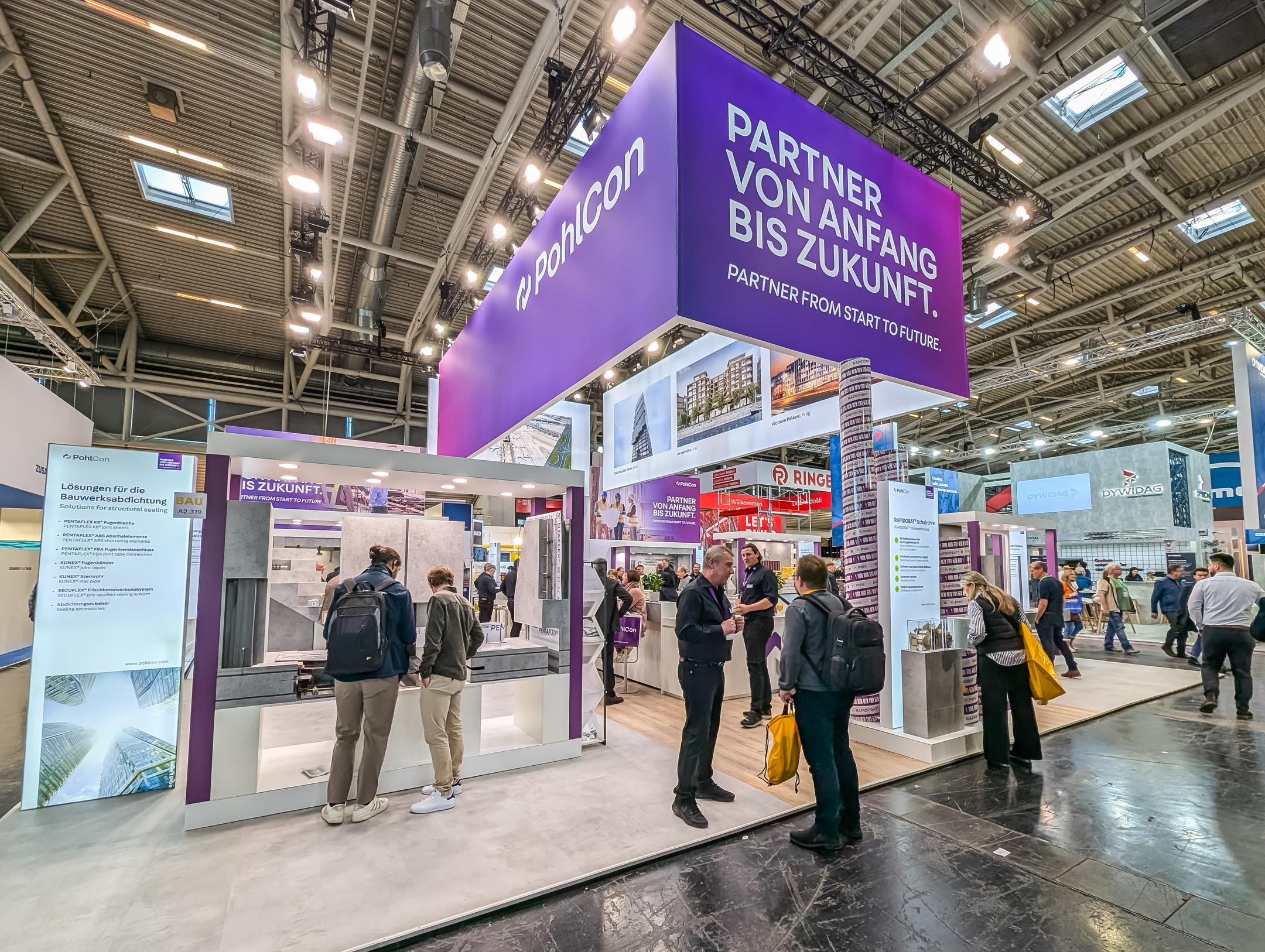 Der gut besuchte Pohlcon-Messestand auf einer Messe. Von der Decke hängt ein lila Banner mit der Aufschrift "Partner von Anfang bis Zukunft".