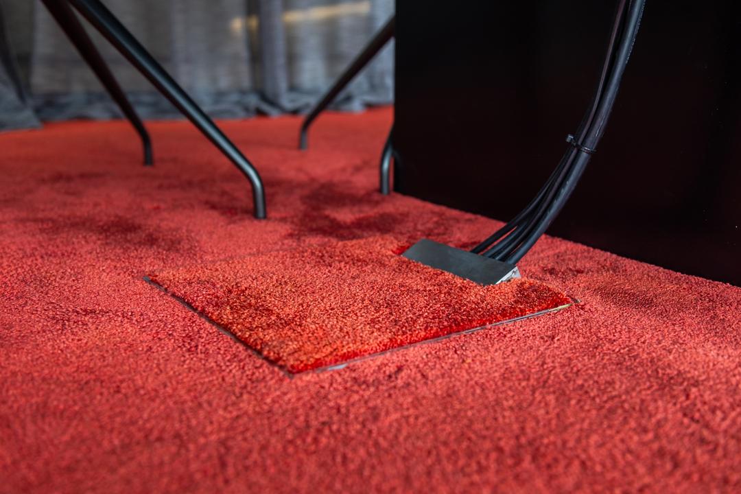 Geschlossenes Bodeninstallationsystem mit Kabelansatz in einem roten Teppich.