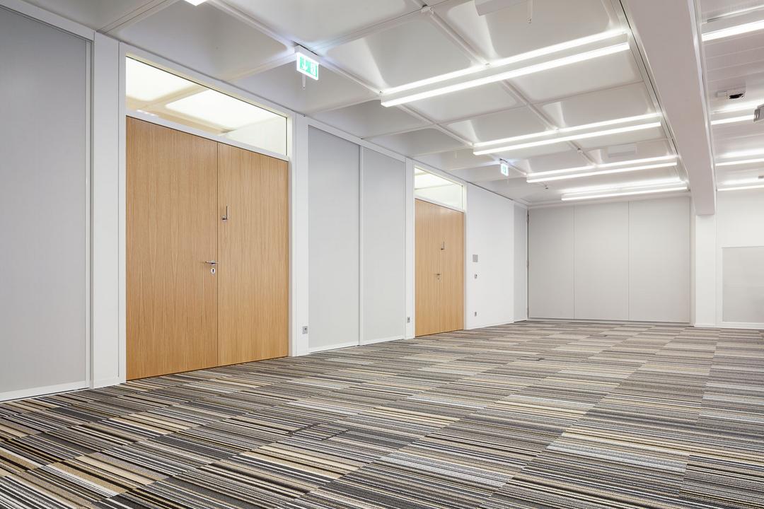 Ein mit Teppich ausgelegter Flur in einem Bürogebäude mit großen Doppeltüren.