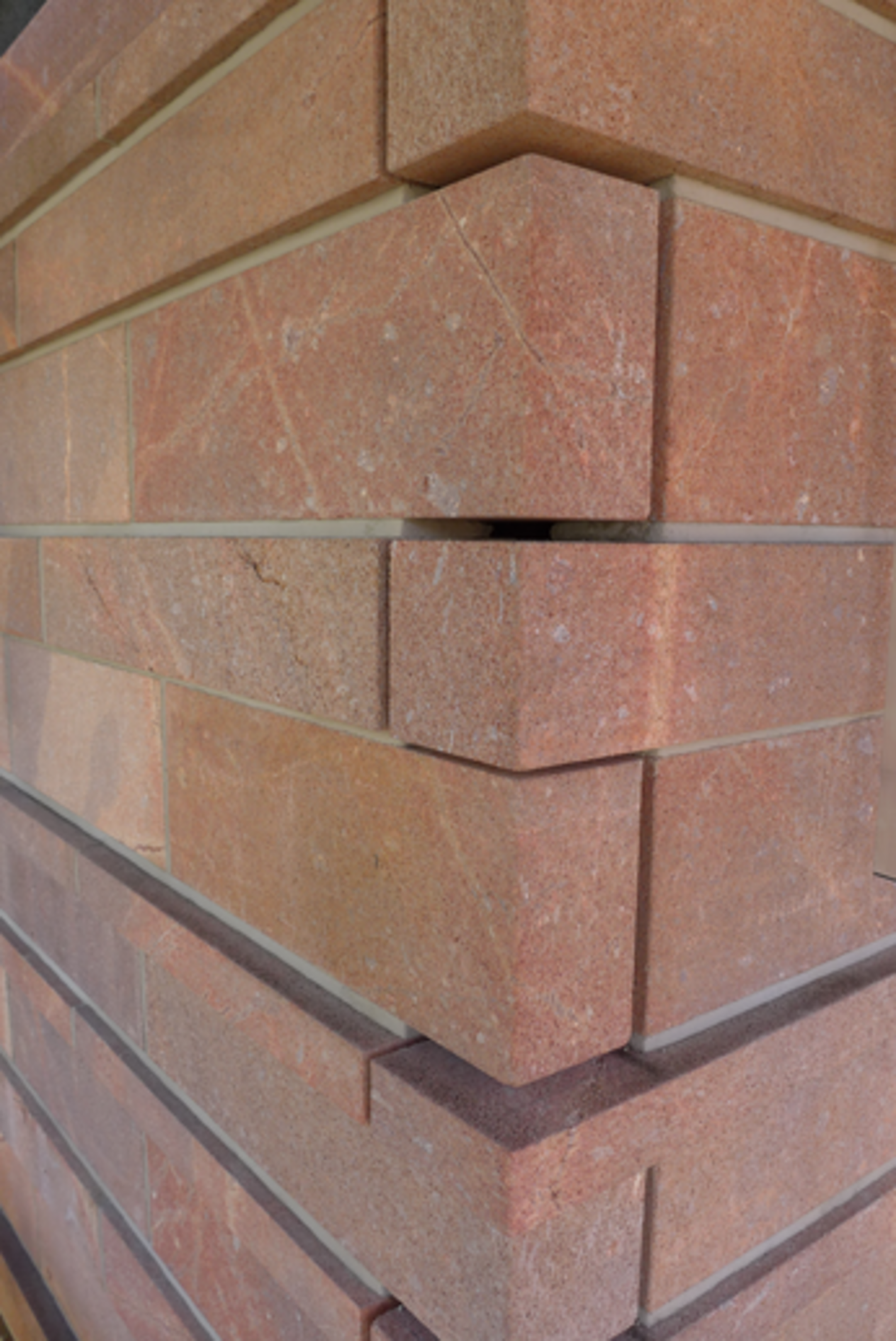 Nahaufnahme einer gemauerten Ecke mit versetzten, rötlich-braunen Steinziegeln in klassischem Verband