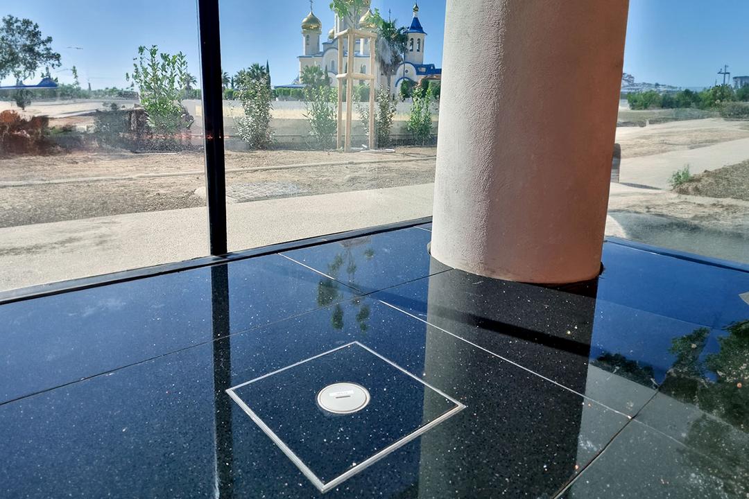 Säule auf schwarzem glänzendem Boden mit Tubusdeckeleinheit vor großem Fenster mit blauen Himmel draußen