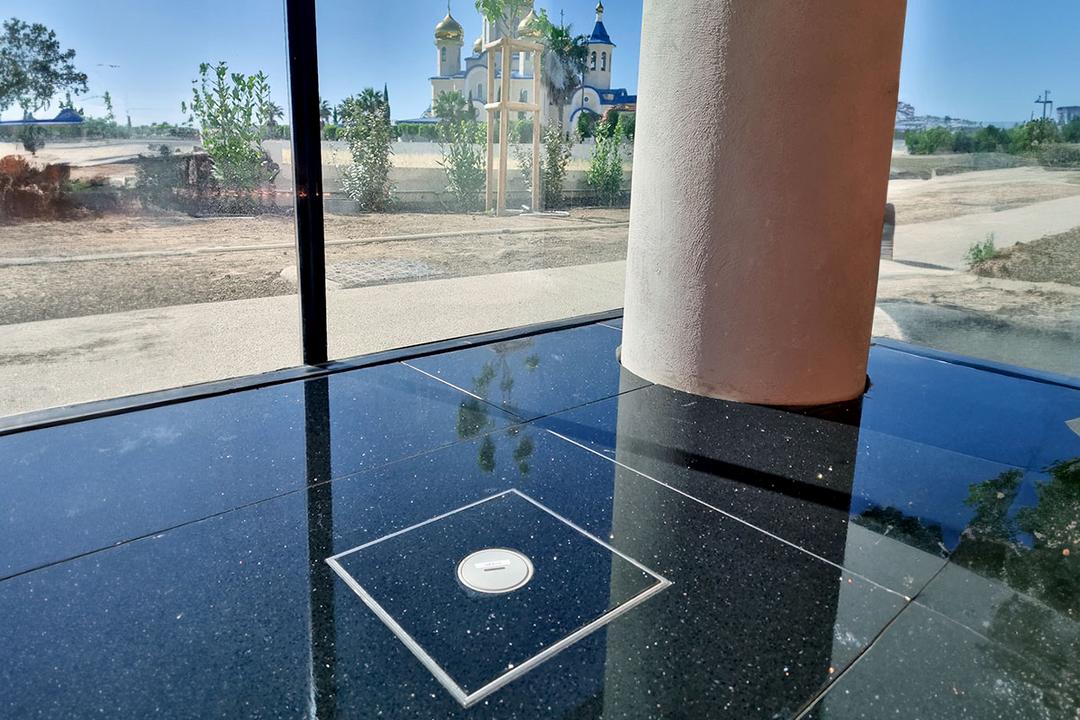 Säule auf schwarzem glänzendem Boden mit Tubusdeckeleinheit vor großem Fenster mit blauen Himmel draußen