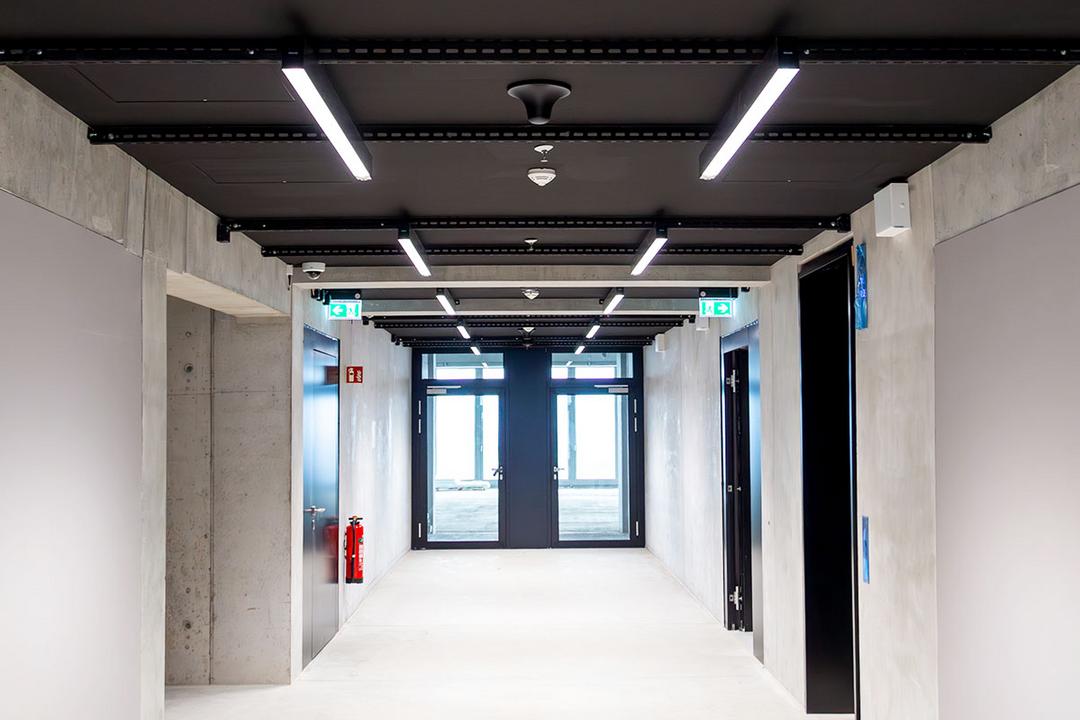 Heller Flur mit Betonwänden, schwarzen Türen, einer schwarzen Decke mit weißen LED-Lichtern und Ausgangstüren am Ende