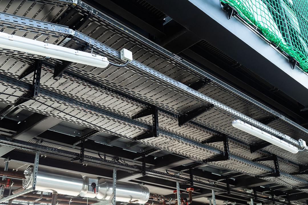 Blick auf eine Baustelle mit schwarzen Kabelrinnen unter einer grünen Schutznetzhängung