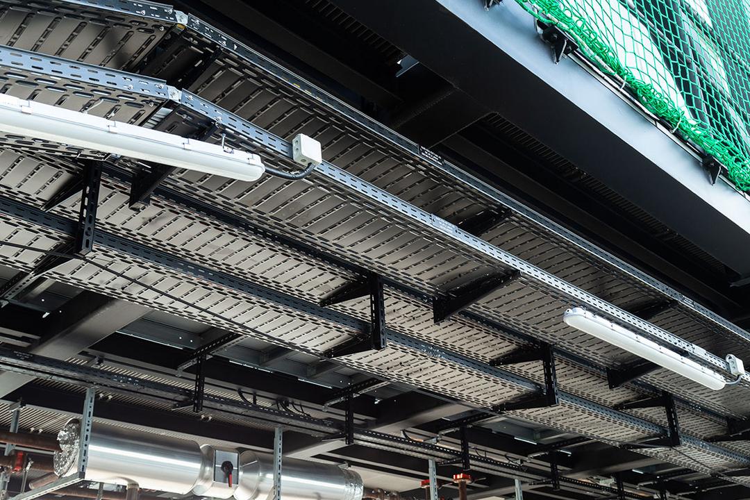 Blick auf eine Baustelle mit schwarzen Kabelrinnen unter einer grünen Schutznetzhängung