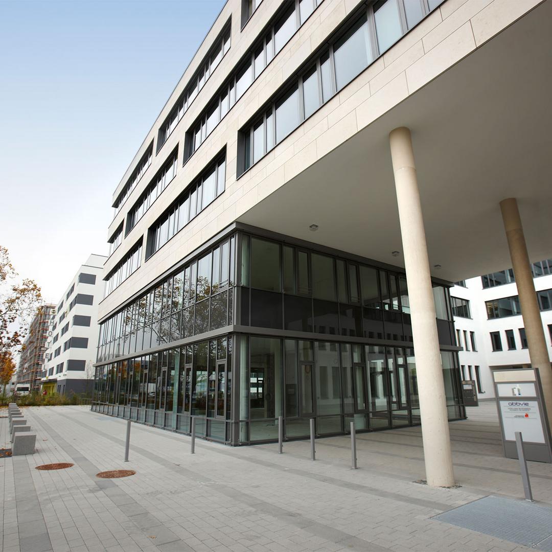 Blick auf ein säulengestütztes, teilverglastes Bürogebäude.