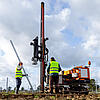 Arbeiter montieren mit Rammmaschine Pfosten für eine Photovoltaik-Freiflächenanlage.