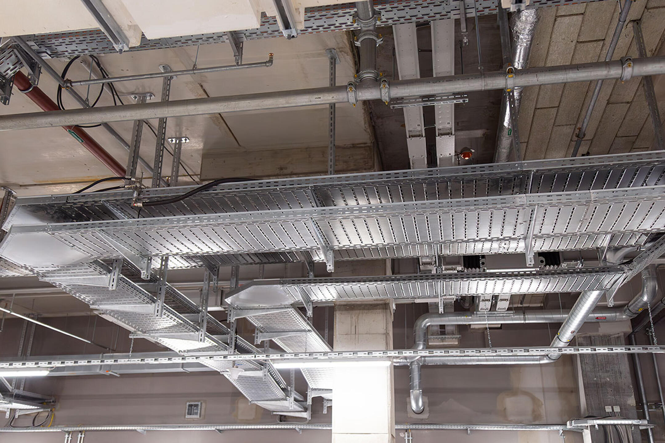 Industrielle Decke mit Kabelrinnen, Rohrleitungen und Betonstützen in modernem Innenraum