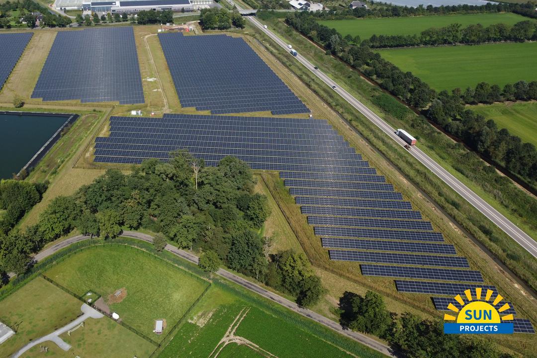 Großflächige Photovoltaikanlage neben Straße und Gewächshaus, aufgenommen aus der Luft.