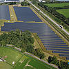Großflächige Photovoltaikanlage neben Straße und Gewächshaus, aufgenommen aus der Luft.