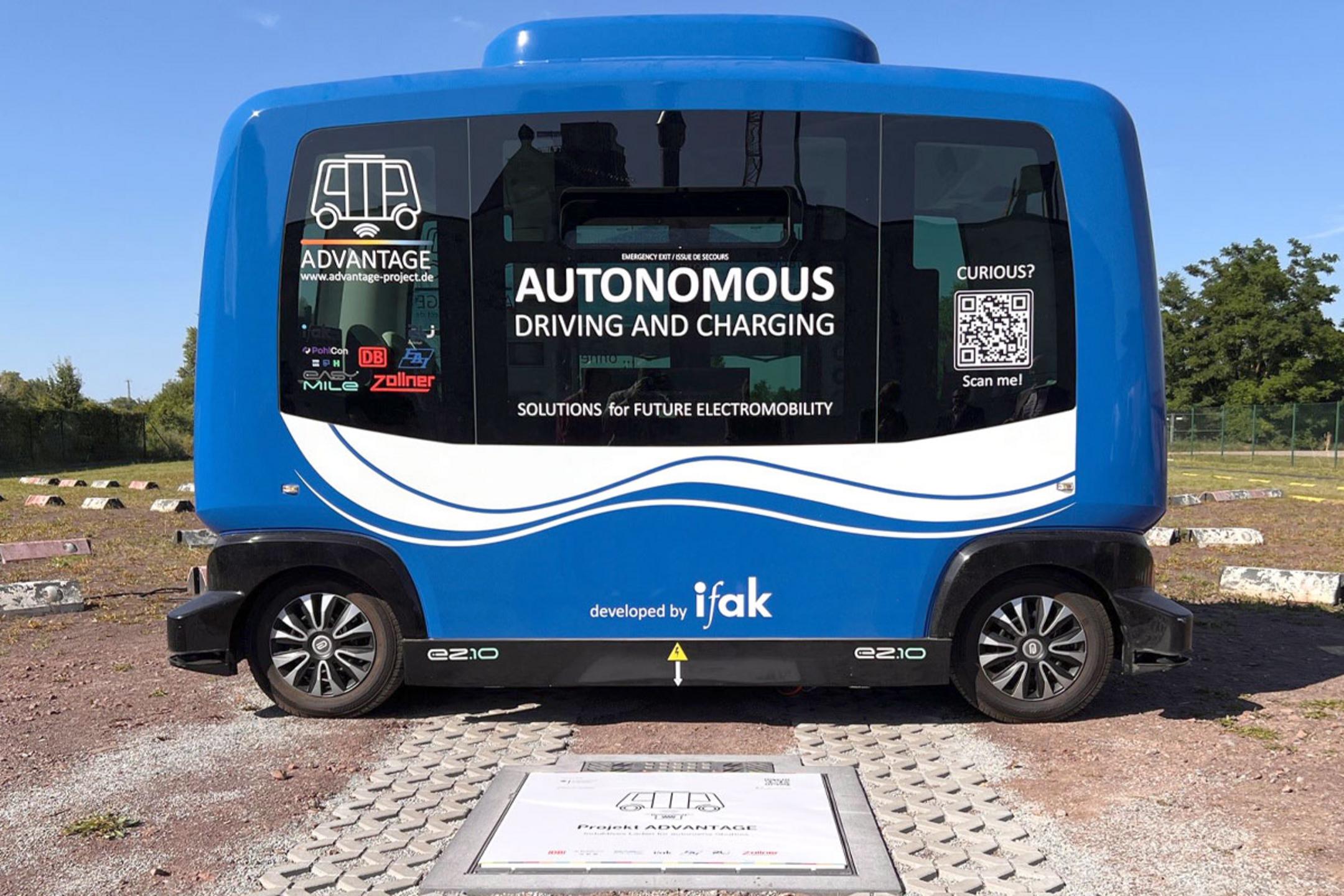 Ein autonomes Shuttle für den öffentlichen Personennahverkehr, das im Freien über einer kontaktlosen Ladestation parkt.