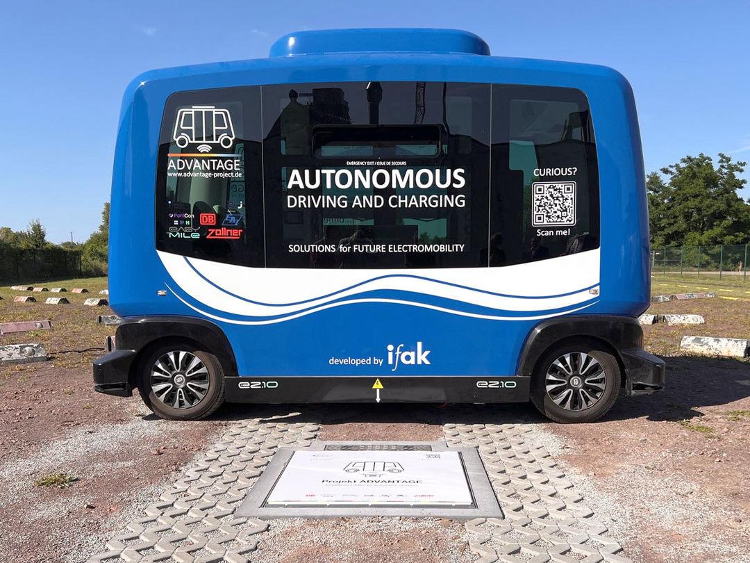 Ein autonomes Shuttle für den öffentlichen Personennahverkehr, das im Freien über einer kontaktlosen Ladestation parkt.