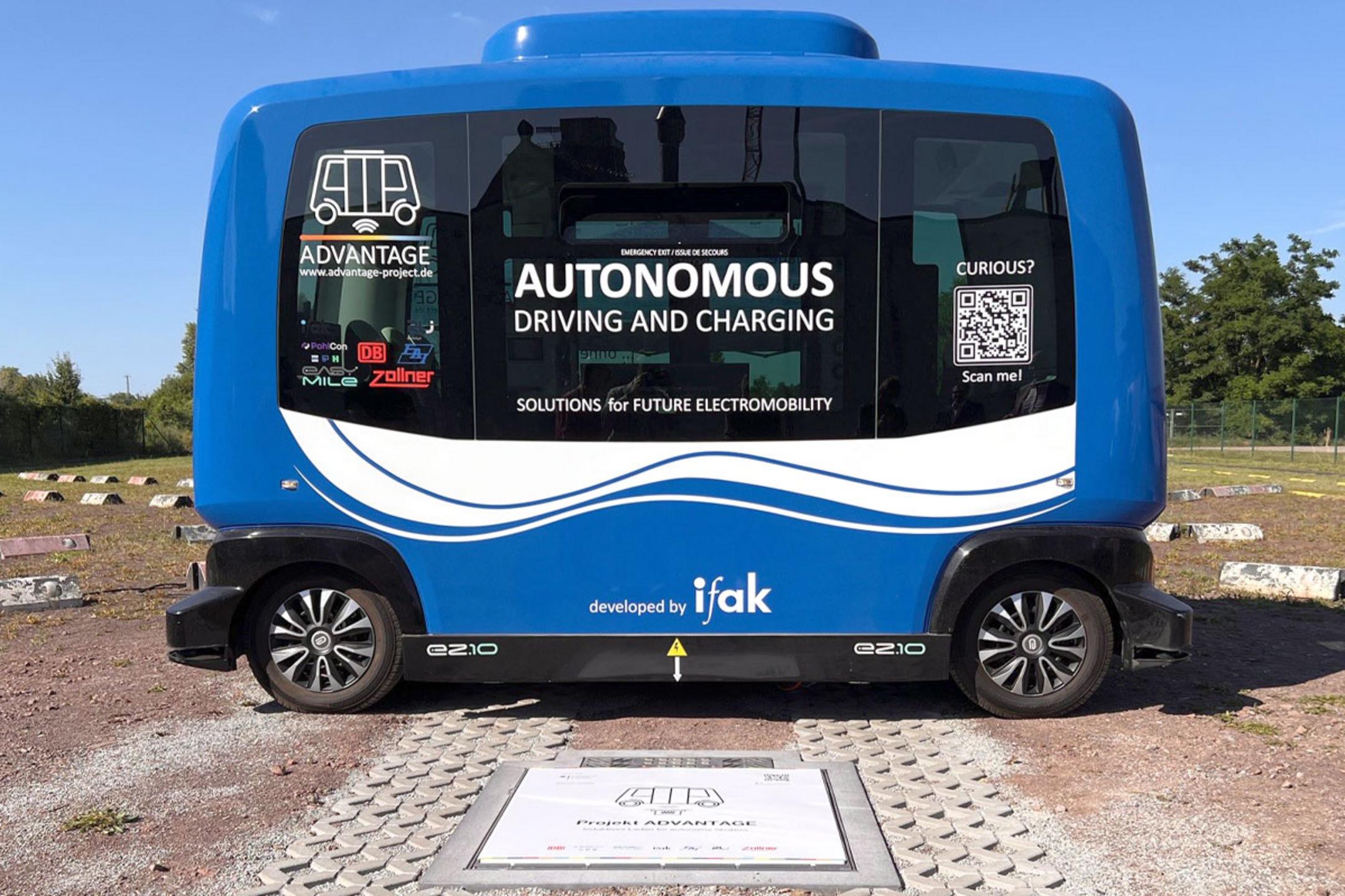 Ein autonomes Shuttle für den öffentlichen Personennahverkehr, das im Freien über einer kontaktlosen Ladestation parkt.