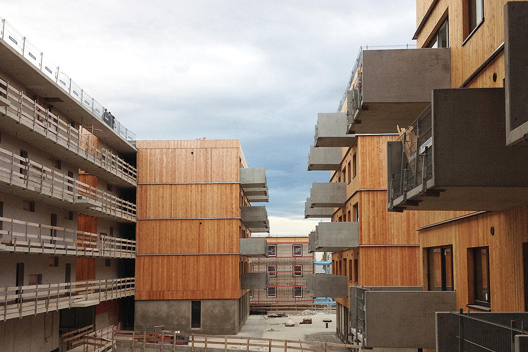 Baustelle mit Blick auf holzverkleidete Gebäude mit herausragenden Balkonen
