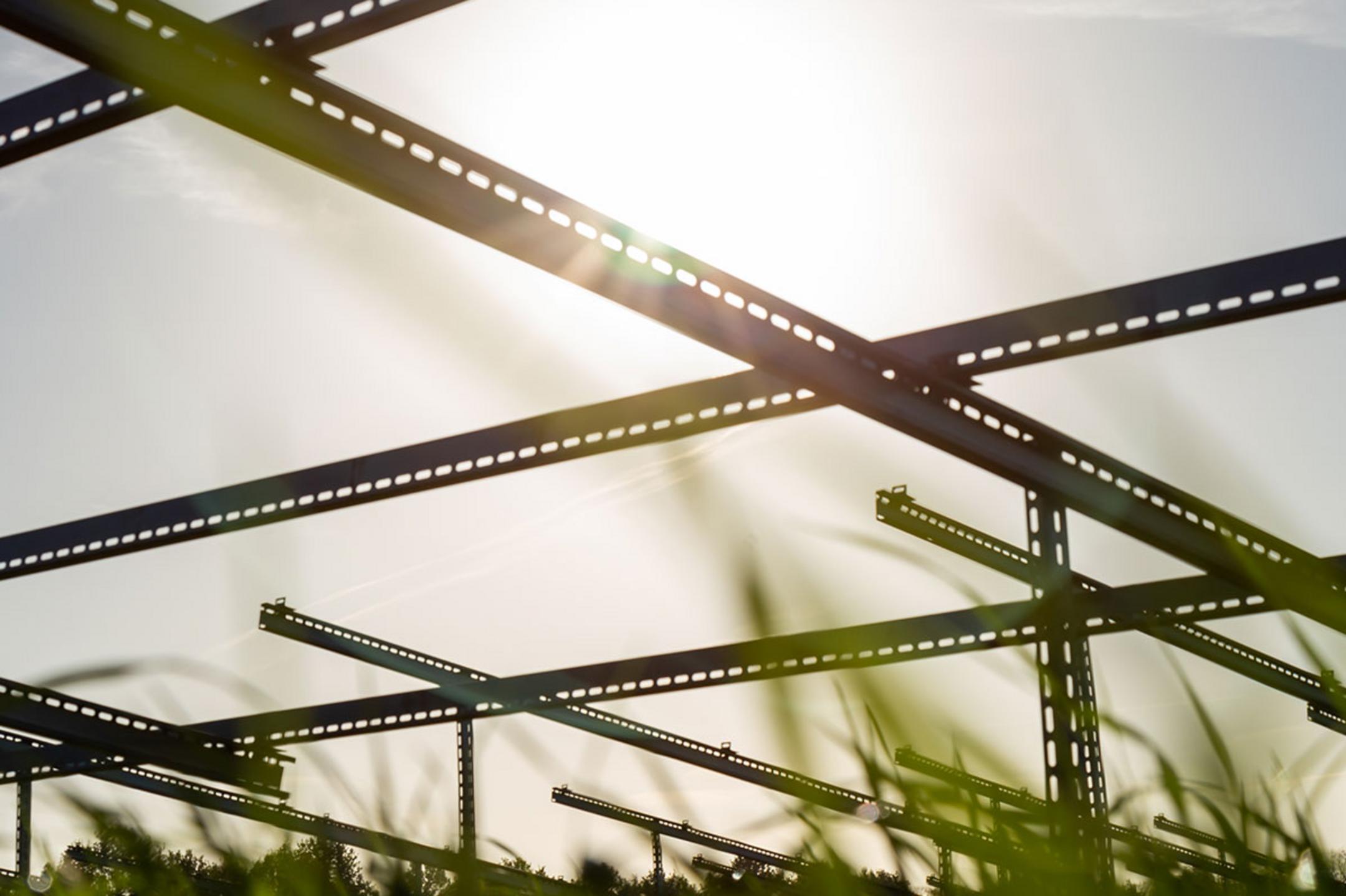 Unterkonstruktionen für Solarpanele aufgenommen aus der Froschperspektive mit Blick in die Sonne und Gras am unteren Bildrand