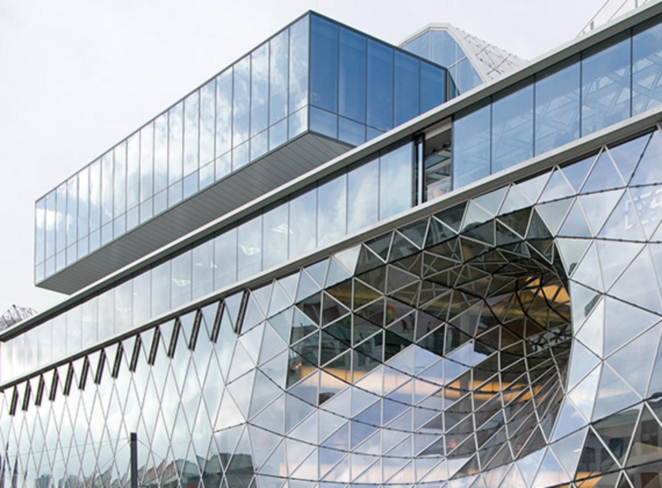 Modernes Gebäude mit Glasfassade, geometrischem Muster und auskragender Glasstruktur mit rundem Ausschnitt