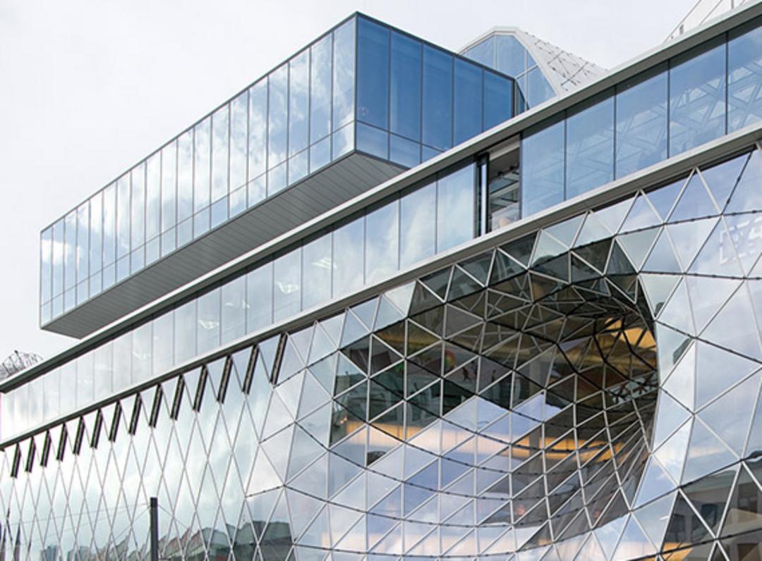 Modernes Gebäude mit Glasfassade, geometrischem Muster und auskragender Glasstruktur mit rundem Ausschnitt