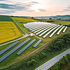 Luftaufnahme einer großen Solaranlage auf Hügeln mit Feldern, Straße daneben, Sonnenaufgang und teils bewölktem Himmel