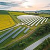 Luftaufnahme einer großen Solaranlage auf Hügeln mit Feldern, Straße daneben, Sonnenaufgang und teils bewölktem Himmel