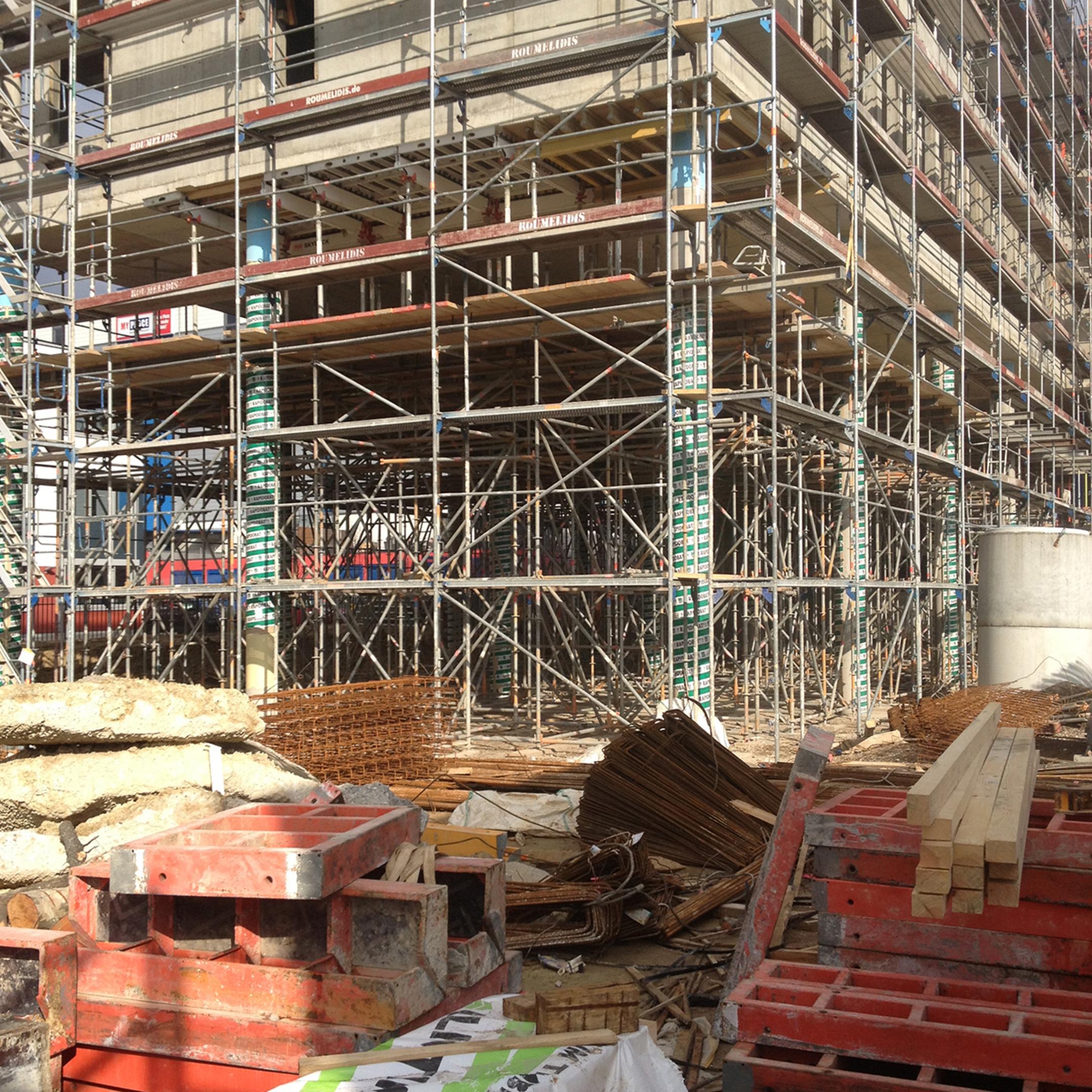 Blick auf eine Baustelle und Baugerüste, mit Materialien und Werkzeugen im Vordergrund.