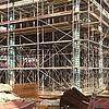 Blick auf eine Baustelle und Baugerüste, mit Materialien und Werkzeugen im Vordergrund.