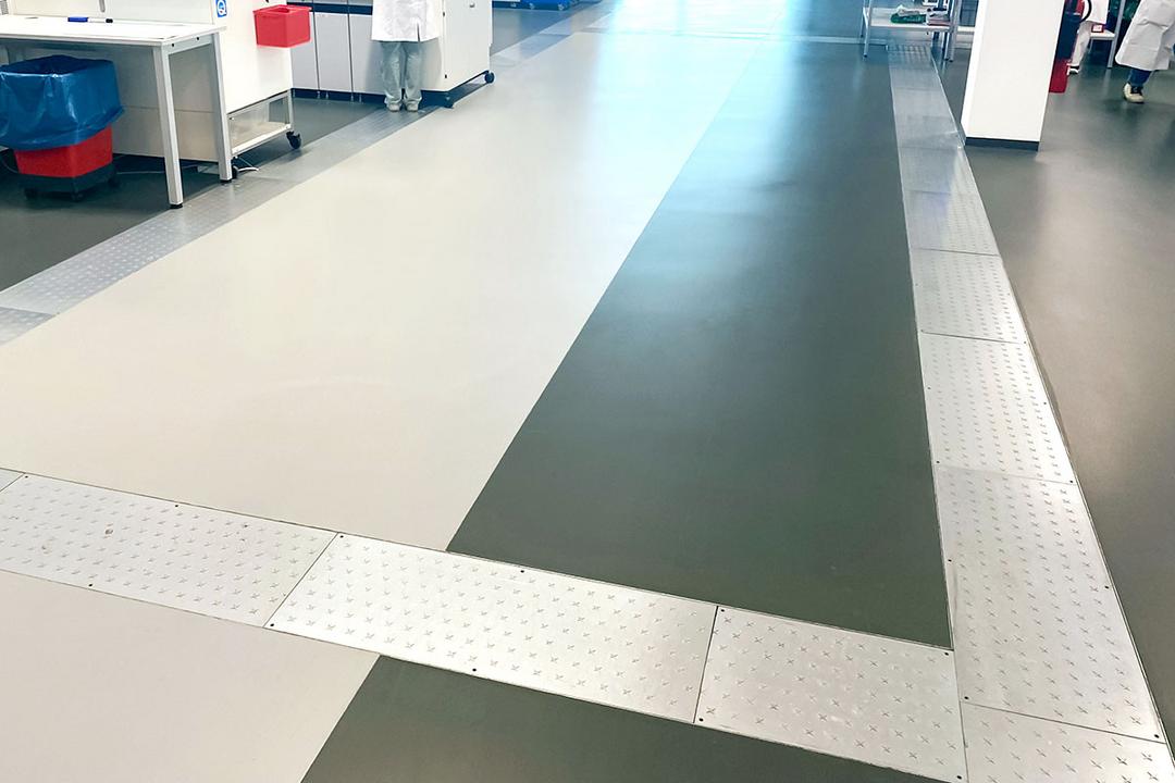 Begehbarer Bodenkanal mit Metallabdeckung in Labor- oder Reinraumumgebung zur verdeckten Leitungsführung.