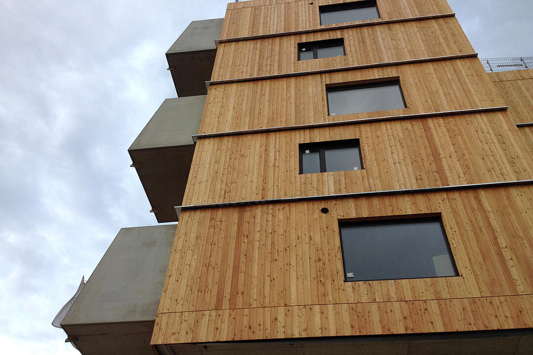 Blick hinauf ein holzverkleidetes Gebäude mit herausragenden Balkonen