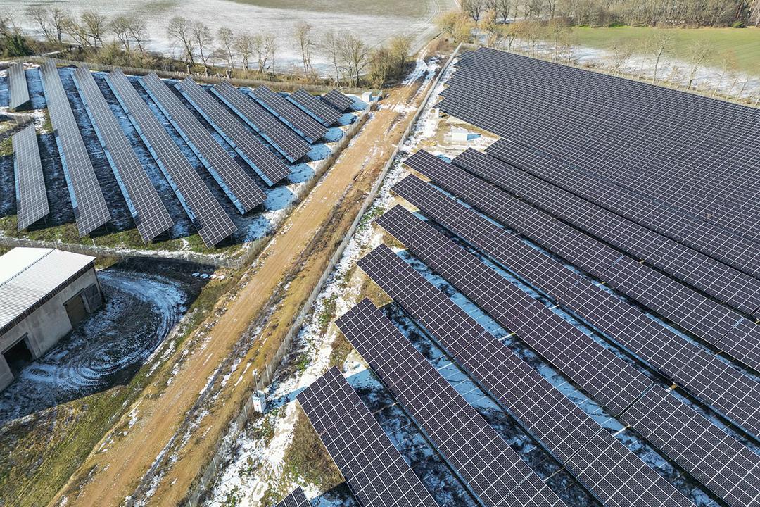 Luftaufnahme eines Solarparks, durch den ein Feldweg führt, Felder grenzen an und sind teilweise von Schnee bedeckt