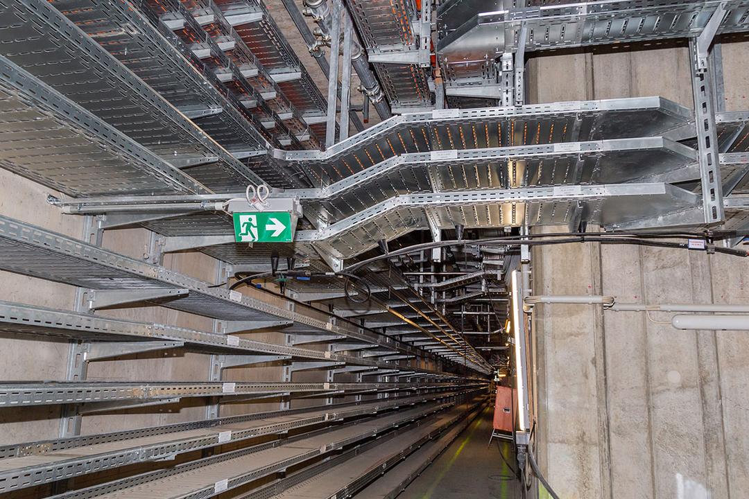 Langer Gang mit Kabelrinnen an der Wand und an der Decke, Notausgangszeichen und Betonwänden in einem Technik- oder Versorgungstunnel