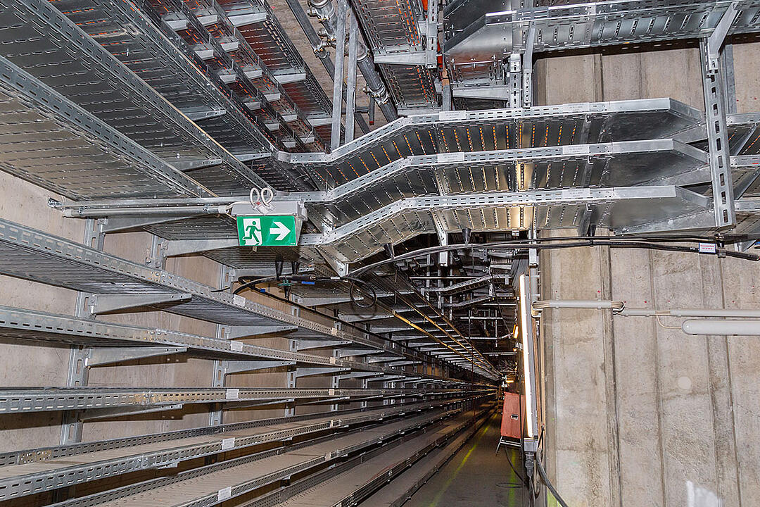 Langer Gang mit Kabelrinnen an der Wand und an der Decke, Notausgangszeichen und Betonwänden in einem Technik- oder Versorgungstunnel