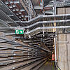 Langer Gang mit Kabelrinnen an der Wand und an der Decke, Notausgangszeichen und Betonwänden in einem Technik- oder Versorgungstunnel