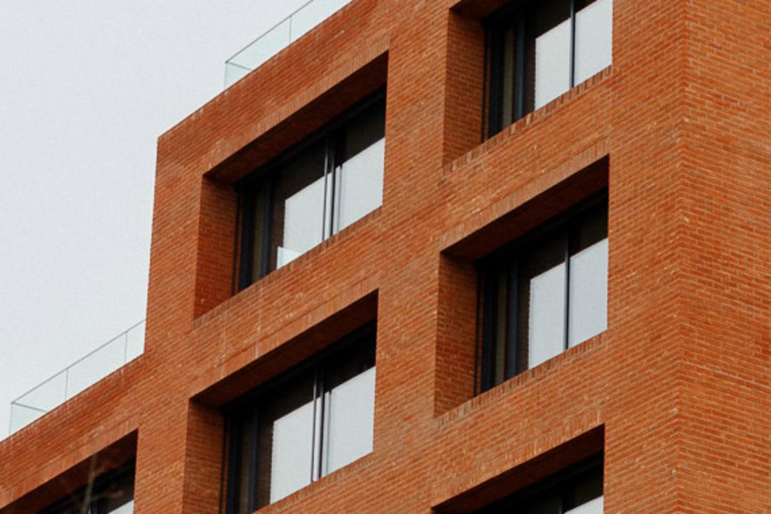Nahaufnahme eines rotes Backsteingebäudes mit Fenstern, bewölkter Himmel im Hintergrund