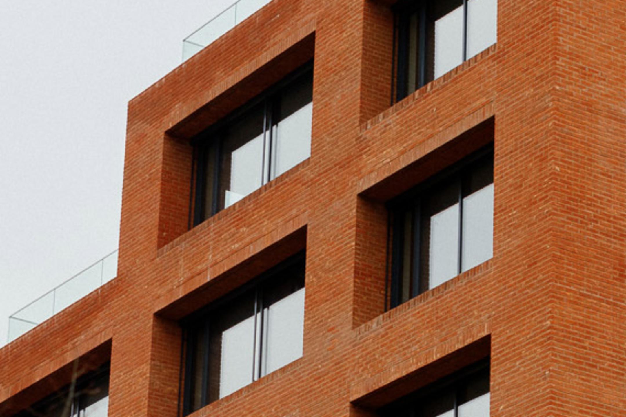 Nahaufnahme eines rotes Backsteingebäudes mit Fenstern, bewölkter Himmel im Hintergrund