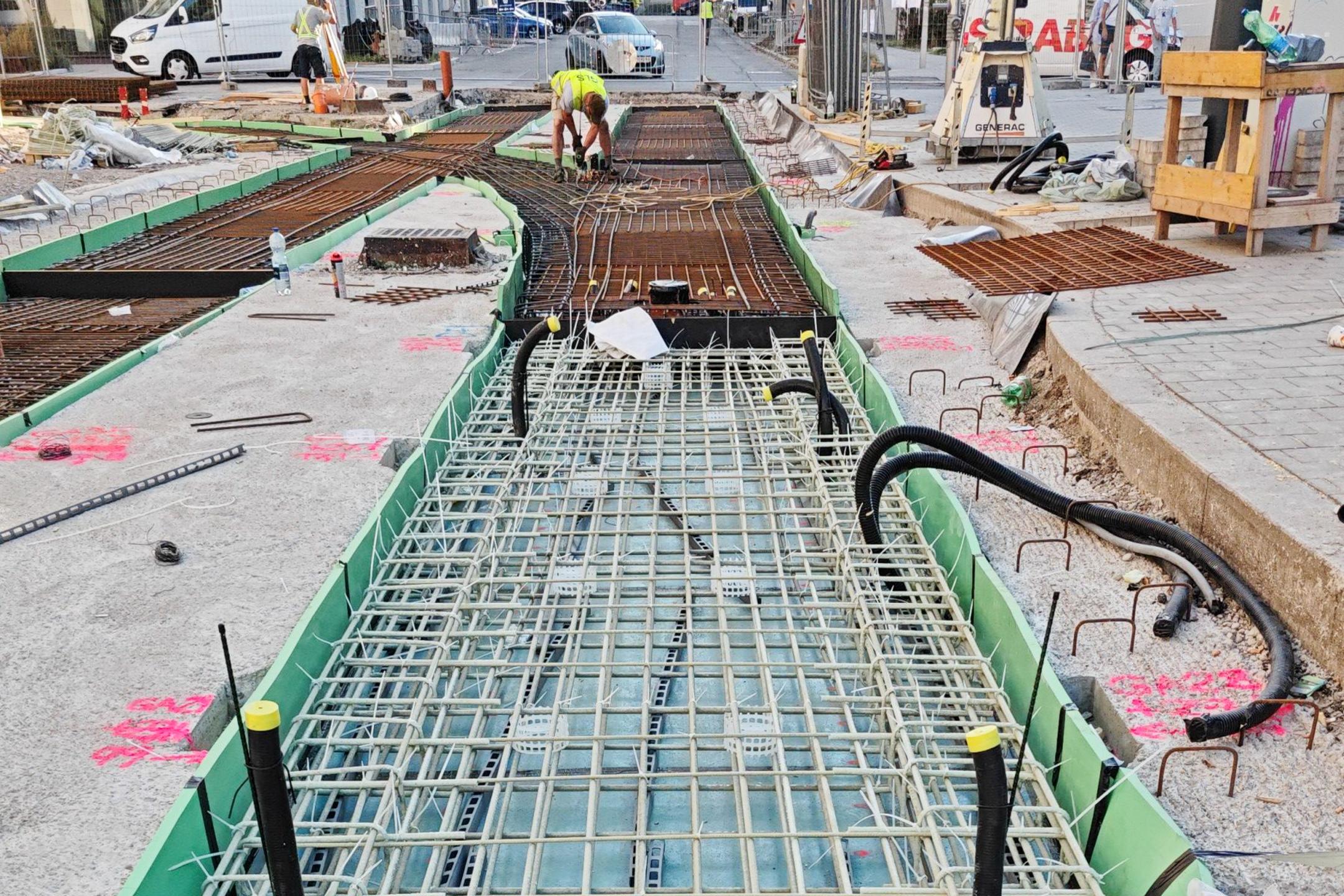 Bewehrungsstäbe aus Glasfaserkunststoff, eingelassen in den Boden auf einer Baustelle, im Hintergrund sind Gebäude zu erkennen