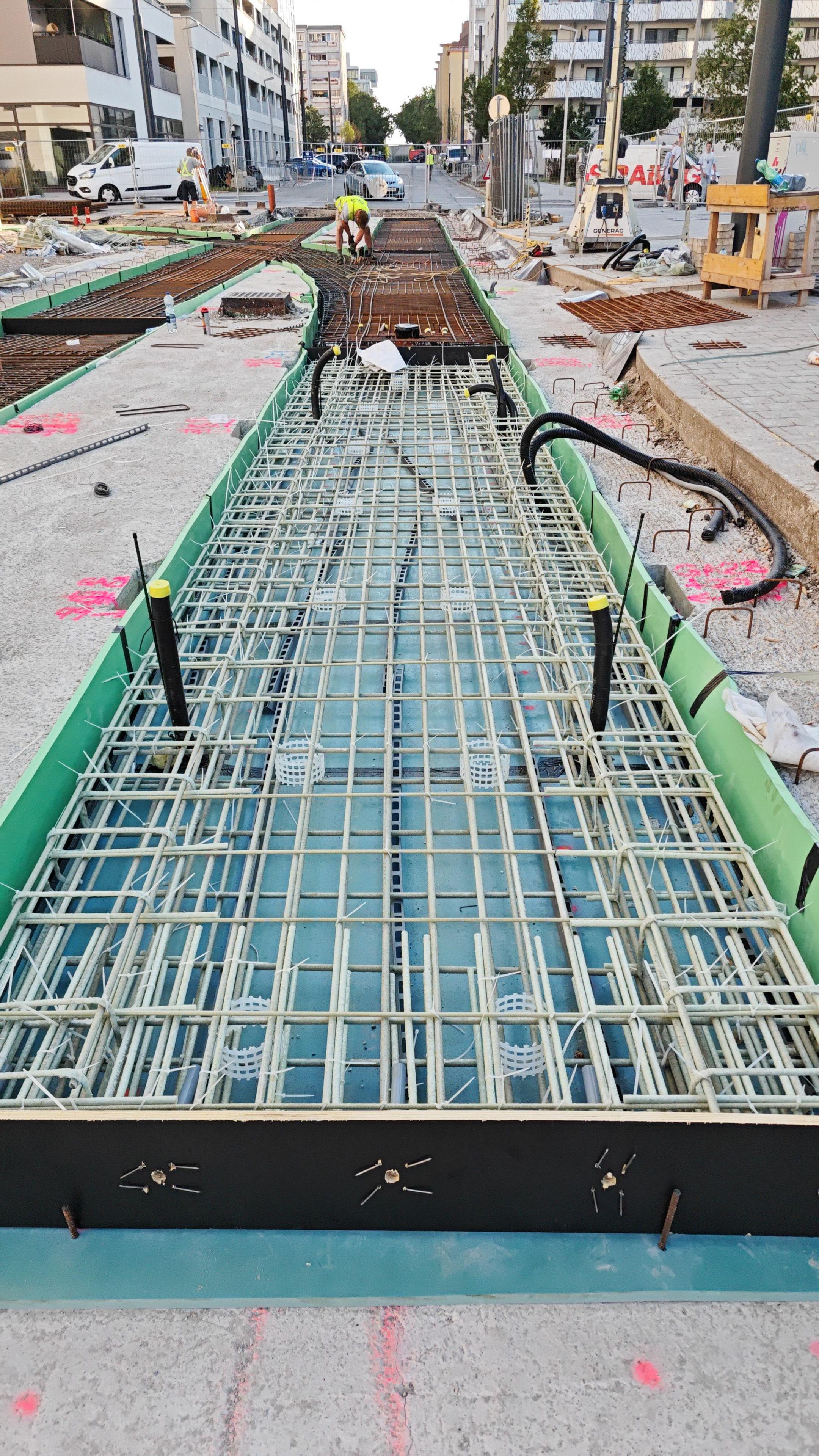 Bewehrungsstäbe aus Glasfaserkunststoff, eingelassen in den Boden auf einer Baustelle, im Hintergrund sind Gebäude zu erkennen