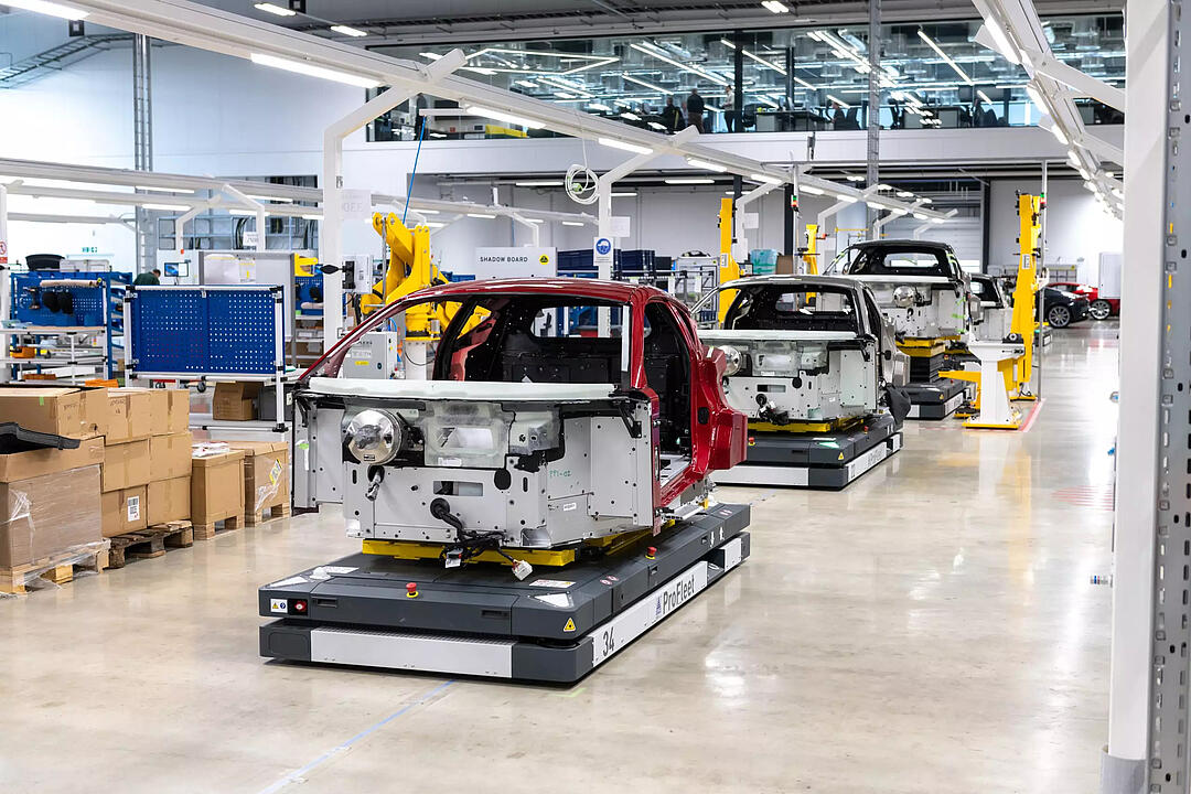 Automatisierte Transportsysteme bewegen Autokarosserien in einer modernen Fertigungshalle, unterstützt von Industrierobotern