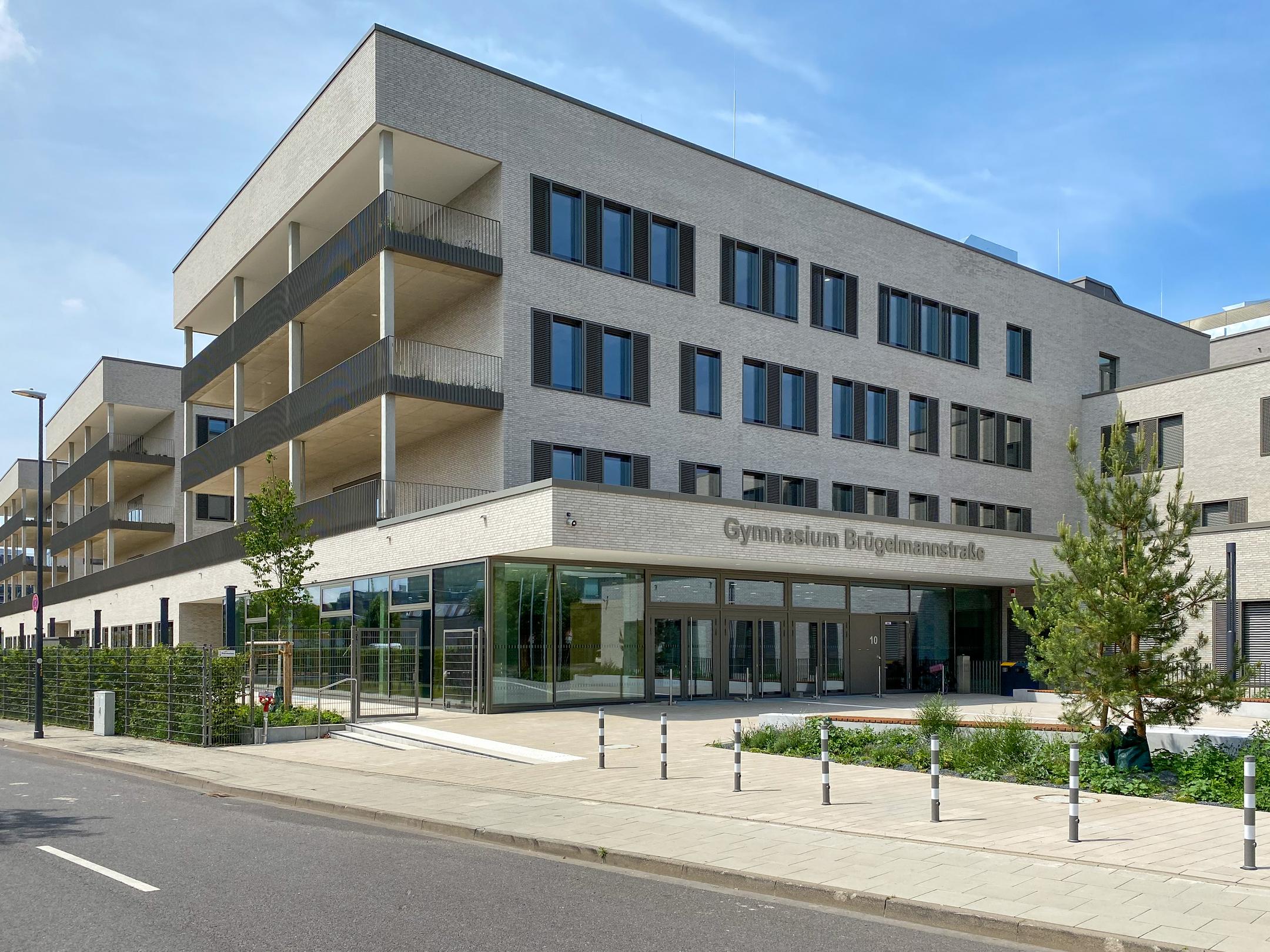 Gebäudeansicht von vorne, Bäume, blauer Himmel, Straße im Anschnitt im Vordergrund