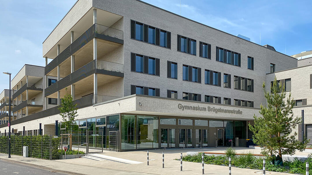 Gebäudeansicht von vorne, Bäume, blauer Himmel, Straße im Anschnitt im Vordergrund