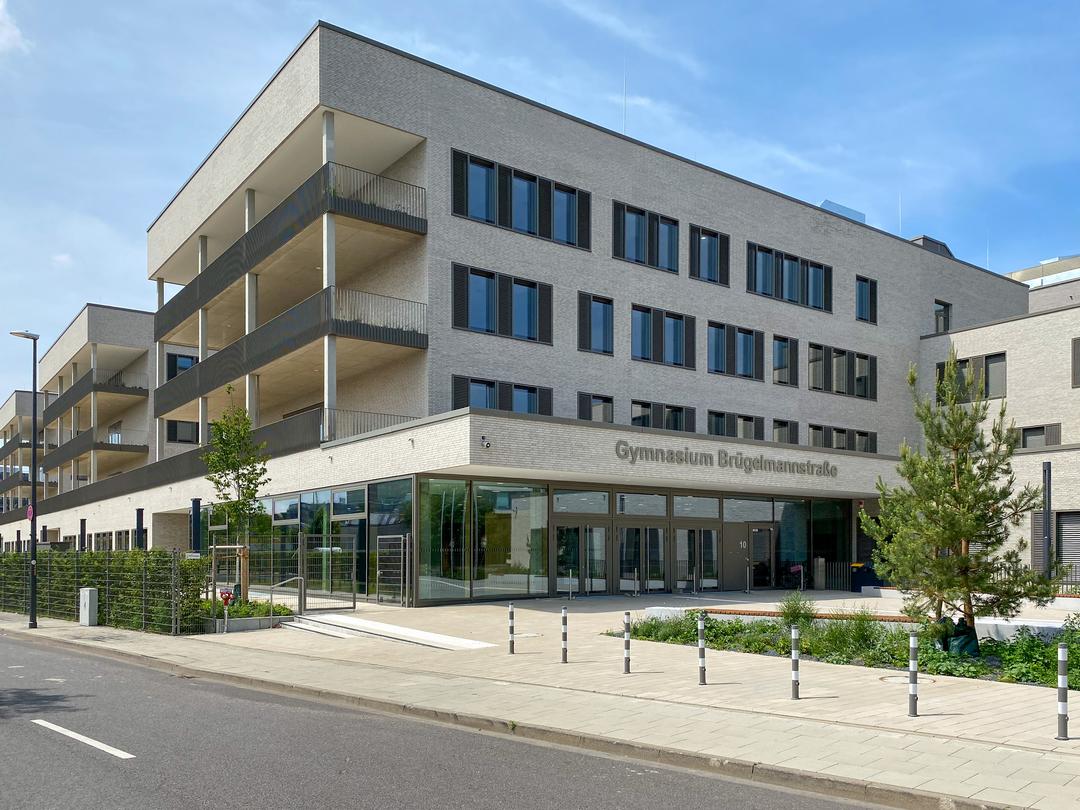 Gebäudeansicht von vorne, Bäume, blauer Himmel, Straße im Anschnitt im Vordergrund