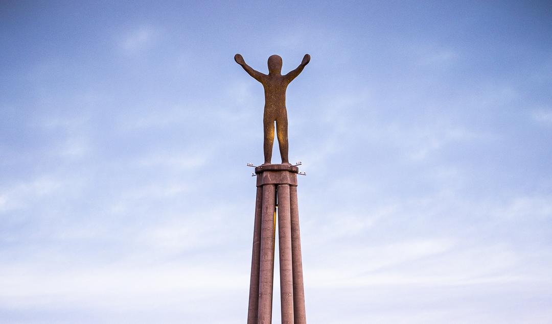 Monument mit erhobener Statue auf Säulenplattform vor blauem Himmel mit vereinzelten Wolken