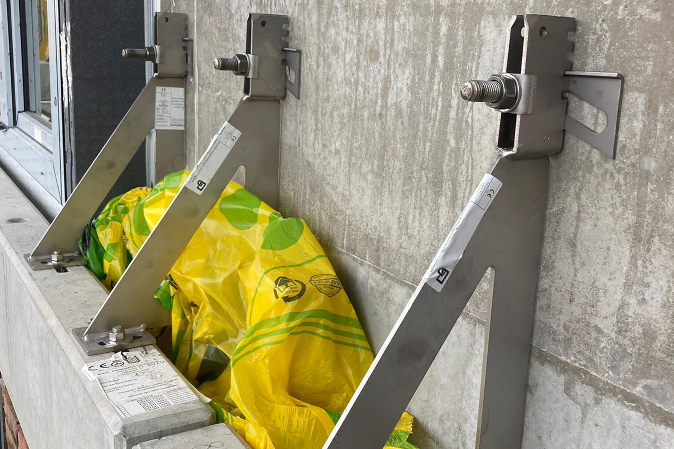 Drei Verblenderkonsolen an einer Betonwand, mit gelbem Kunststoff und Bauelementen im Hintergrund