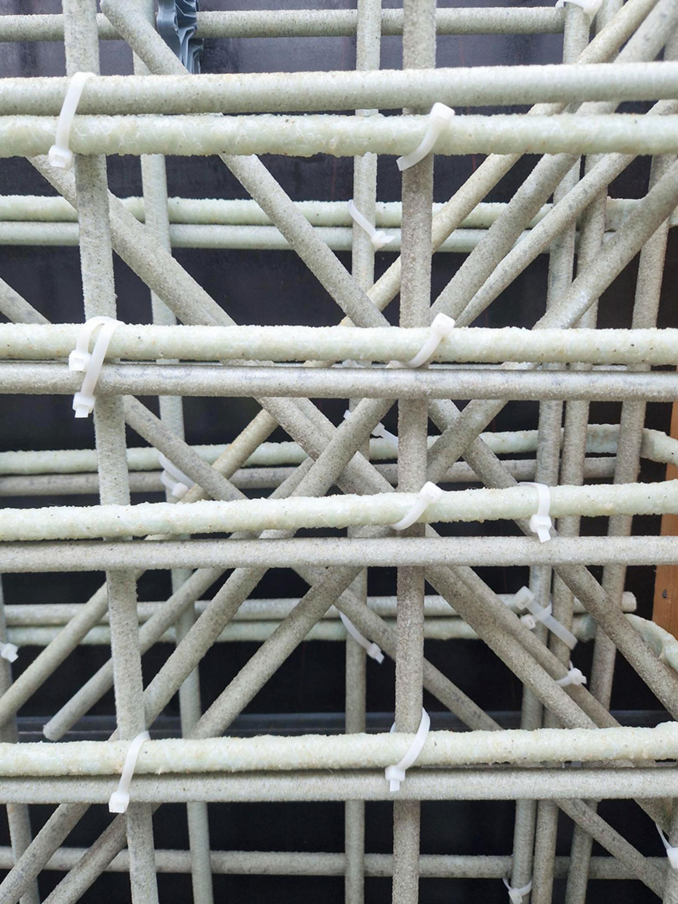Nahaufnahme einer Glasfaserkunststoffbewehrung mit Kabelbindern fixiert, vor schwarzer Schalung