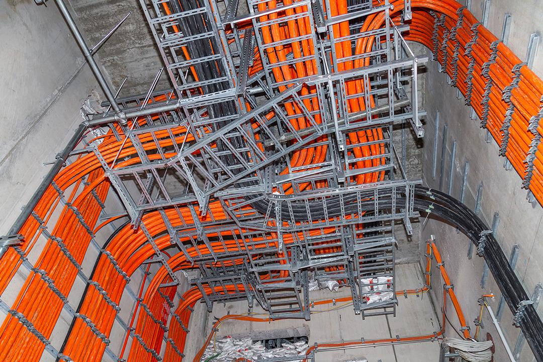 Installierte Kabelleitern mit dicken orangefarbenen und schwarzen Kabeln in einem Raum mit Betonwänden